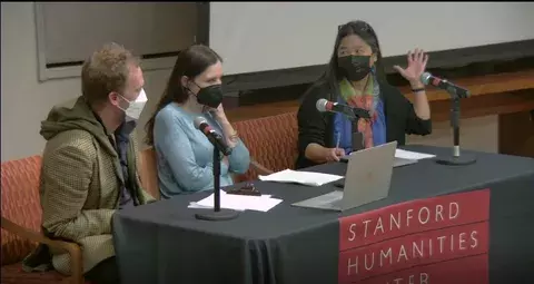 Group of three people sit at a table, wearing masks.